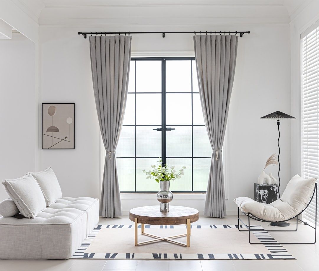 Lyst oppholdsrom med tunge gardiner, sofa, stol og teppe